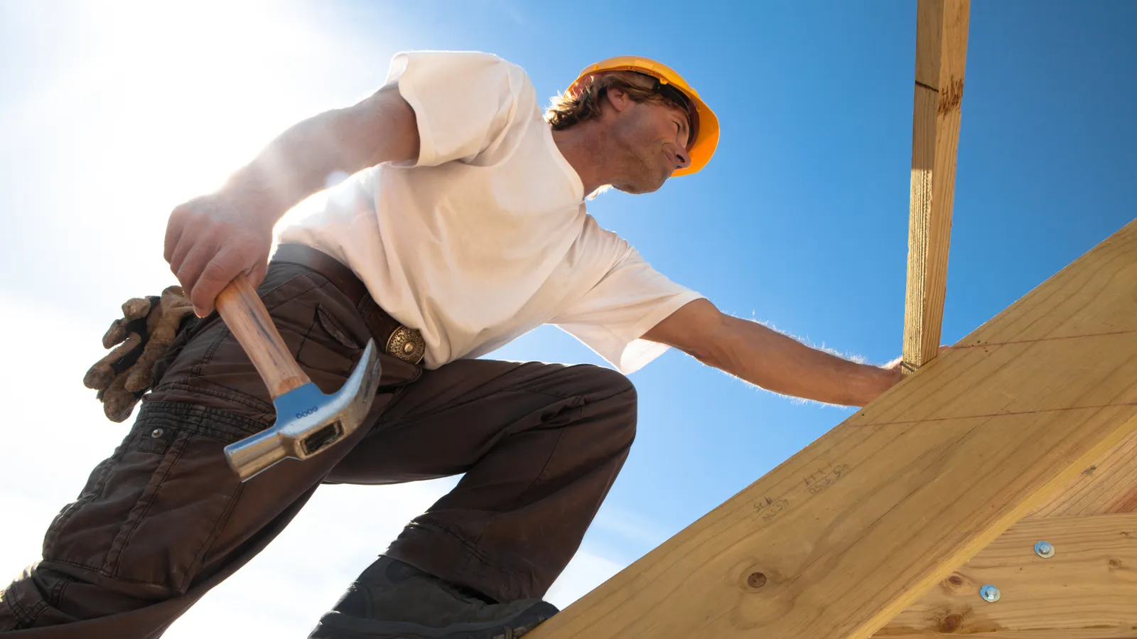 Wooden roof framing climbed by a roofer holding a hammer